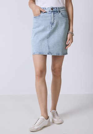 Helles blauer Denimrock mit enger Passform, hoher Taille und sanften Ausbleichungen; verfügt über frontale Taschen und eine Länge bis zur Mitte des Oberschenkels. Kombiniert mit weißen Sneakers.