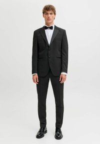 Mustast satiinist revääridega smoking, valgekleit särk, must kikilips ja mustad kingad. Kohandatud lõige, minimalistlik disain ja elegantne välimus.