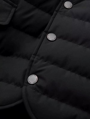 Chaqueta acolchada negra con un diseño de acolchado, que presenta un cuello redondeado, botones a presión y una textura de tela suave y resistente al agua.