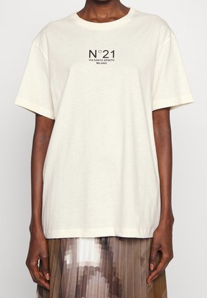 Persoon draagt een los wit T-shirt met "N°21 VIA SANTO SPIRITO MILANO" in het zwart gedrukt op de borst en een geplooide rok.