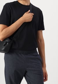 Svart kortärmad t-shirt, avslappnad passform, i kombination med texturerade mörkblå byxor med elastisk midja. Liten svart axelväska.