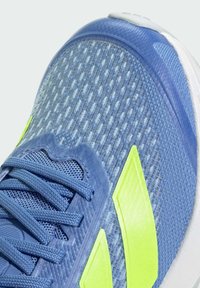 Blauwe sport schoen met een geperforeerde mesh bovenkant, groene accenten en smalle veters. Witte zool met een lichte kromming. Geen zichtbaar logo.