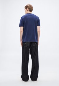 Bombažno majico mornarsko modre barve s kratkimi rokavi, kombinirano z ohlapnimi temno modrimi kavbojkami z dvema zadnjima žepoma in rumenim vezenjem.