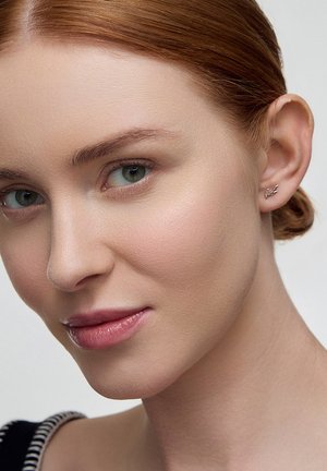 Srebrny klips na ucho na modelce. Gładki, minimalistyczny design o subtelnym falistym kształcie. Modelka ma jasną skórę i proste, kasztanowe włosy.