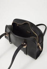 Borsa a mano in pelle nera con zip e accessori dorati, dotata di due manici e un interno aperto che mette in mostra una tasca piccola e una superficie liscia.