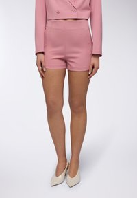 Shorts rosa su misura con una consistenza liscia e design aderente. Indossati con tacchi a punta in crema, che mostrano uno stile minimalista.