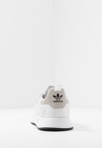 Valkoinen urheilukenkä, jossa on teksturoitu kangaspäällinen, mokkanahkainen kantapää ja musta logo. Kenkässä on vedinjälki ja kontrastivärinen musta ulkopohja.