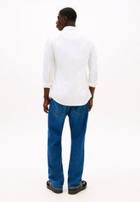 Camisa branca de manga comprida, corte descontraído; combinada com jeans azuis, perna reta, bolsos clássicos; sandálias pretas completam o conjunto.