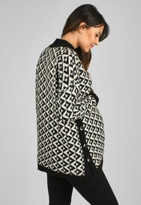 Sweter z dzianiny z czarno-białym geometrycznym wzorem, z długimi rękawami, ściągaczami przy mankietach oraz zapinanymi bocznymi otworami umożliwiającymi regulację dopasowania.