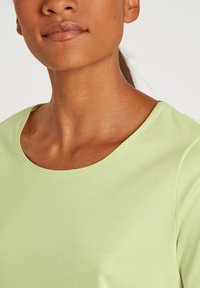 Lichtgroene top met korte mouwen, een ronde halslijn en een gladde stofstructuur, die een eenvoudig, modern ontwerp laat zien.