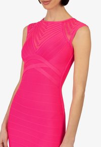 Tailliertes Kleid in leuchtendem Pink, mit gerippter Textur und vertikalen sowie diagonalen Linien. Ärmelloses Design mit Rundhalsausschnitt.