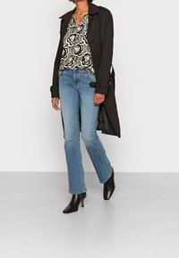 Cappotto nero sopra una blusa a fiori, abbinato a jeans flare blu chiaro e stivaletti neri a punta.
