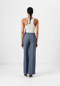 Hochtaillierte, weit geschnittene Hose aus einem strukturierten blauen Stoff, kombiniert mit einem figurbetonten weißen Tanktop. Glatte Oberfläche ohne sichtbare Muster oder Akzente.