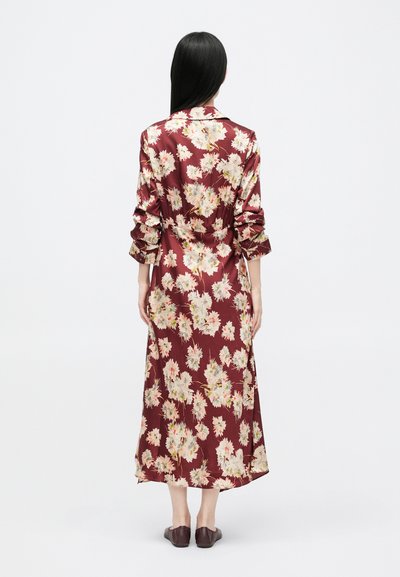 Bordowa sukienka w kwiaty z długimi rękawami i paskiem do wiązania. Materiał o satynowym wykończeniu i luźny krój, z białymi i żółtymi kwiatami na całej powierzchni.