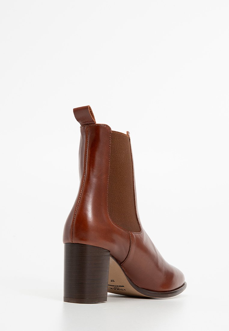 Stivale alla caviglia in pelle marrone con punta arrotondata, pannelli laterali elastici e tacco di legno spesso. Presenta dettagli di cucitura e una linguetta per il movimento.