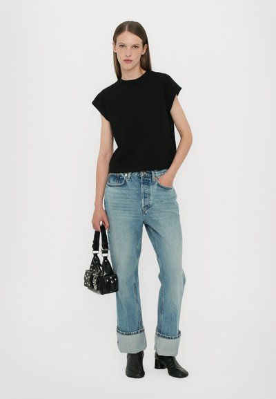 Black, short-sleeve, cropped top paired with light-wash, loose-fitting jeans rolled at the cuffs, and a small black handbag with silver accents.