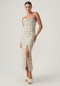 Abito midi con scollo a cowl, in tessuto verde chiaro a fantasia, con spacco laterale e spalline sottili. Modella che indossa sandali con tacco off-white.