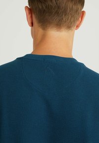 Mörkblå texturerad sweatshirt med rund hals och en liten broderad detalj nära kragen. Vaffelstickad tyg ger ett upphöjt mönster.