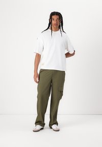 T-shirt blanc surdimensionné, à manches courtes, avec une étiquette sur l'ourlet. Pantalons cargo vert olive avec poches latérales. Baskets blanches avec des accents marron.