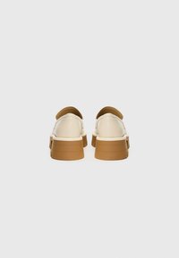 Scarpe con tacco chunky, con una tomaia crema e dettagli marroni. Materiale in pelle liscia, forma arrotondata e design della suola a strati molto evidente.