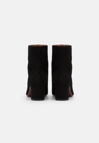 Stivaletti neri in suede con finitura testurizzata, tacco medio a blocco e cuciture laterali, che mostrano l'interno in pelle naturale e i dettagli di costruzione.