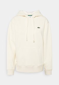 Krémově zbarvená mikina s kapucí, přední kapsou ve stylu klokánka, šňůrkou na stažení kapuce a vyšívaným zeleným krokodýlem na hrudi. Měkká, texturovaná látka.