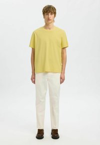 T-shirt en coton jaune avec un col rond, associé à un pantalon crème et des chaussures marron. Simple, coupe décontractée sans motifs ni accents.