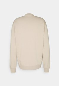 Beige sweatshirt met lange mouwen, een ronde hals en geribbelde boorden. Gladde textuur, eenvoudig ontwerp zonder patronen of accenten.