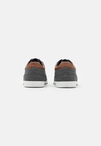 Grå sneakers med brune læderdetaljer, der har et tekstureret stof, glat hvid sål og et lavtop-design.