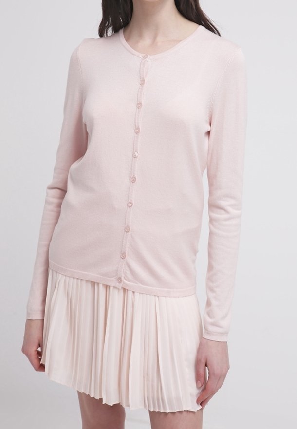 Cardigan rosa claro hecho de tela suave, con un escote redondo, mangas largas y un cierre frontal de seis botones. Combinado con una falda plisada.