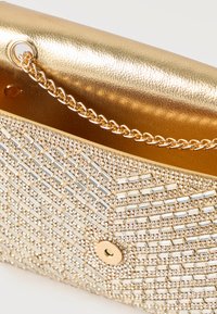 Bolso clutch dorado con correa de cadena, decorado con piedras brillantes rectangulares y redondas transparentes, mostrado abierto sobre un fondo blanco.
