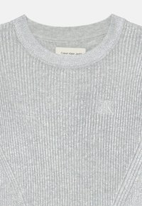 Maglione argentato a coste con scollo a girocollo e un sottile dettaglio del logo. La texture è morbida con un effetto lucido, offrendo una silhouette aderente.