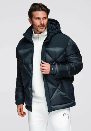 Takkia sinisessä, jossa on huppu, ja jossa on tikattu muotoilu sekä vetoketjut edessä. Hihansuissa on napit ja hihassa on logo koristeena.