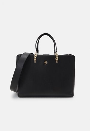 Zwarte leren handtas met twee bovenhandvatten, een brede schouderriem en gouden ketting- en logodetails op een effen achtergrond.