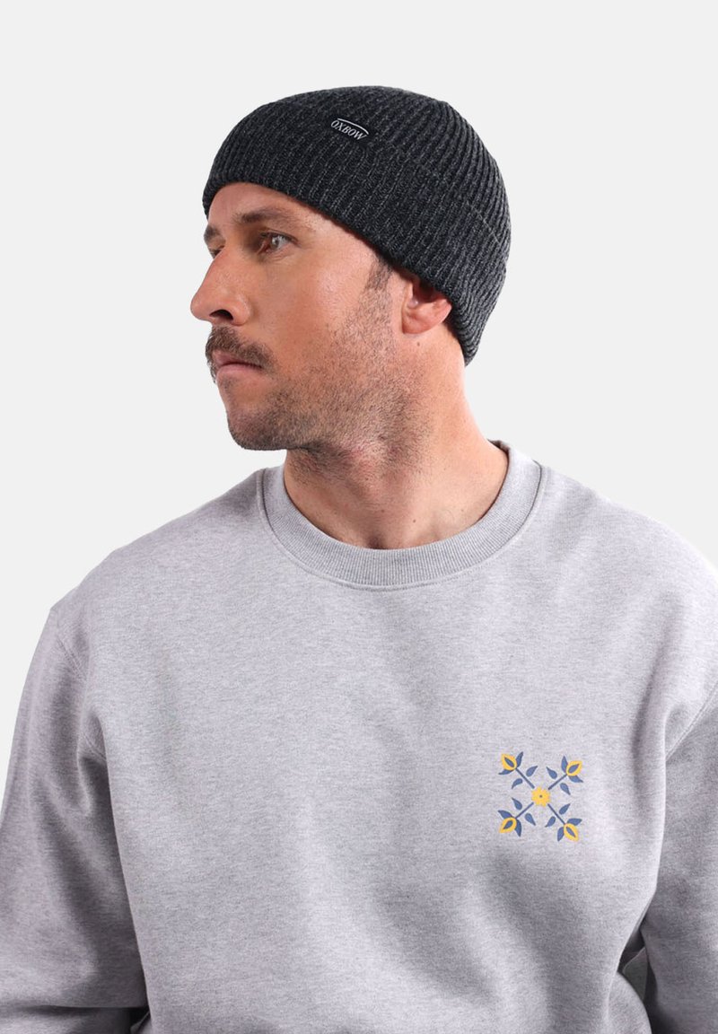 Bonnet en tricot gris avec une texture côtelée, associé à un sweat-shirt gris orné d'un motif floral en bleu et jaune.