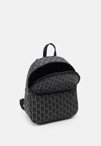 Czarny plecak z białym geometrycznym wzorem, górny uchwyt, przednia kieszeń na zamek błyskawiczny oraz częściowo otwarta główna komora na białym tle.