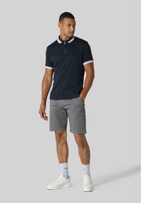 Polo blu navy con dettagli bianchi, maniche corte; abbinato a pantaloni grigi e sneakers bianche. Tessuto morbido, vestibilità classica, design minimal.