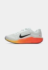 Zapatilla de correr Nike de malla blanca con un swoosh negro y una suela en degradado multicolor (de naranja a amarillo) que presenta una parte superior texturizada y cordones.