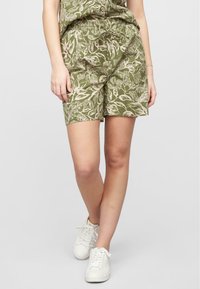 Shorts verts en tissu léger avec un motif de feuilles blanches, taille élastique et coupe décontractée. Les chaussures sont des baskets blanches.
