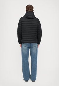 Jachetă puffer neagră cu cusături orizontale, glugă și croi relaxat. Asortată cu blugi evazați, cu talie înaltă, din material denim.