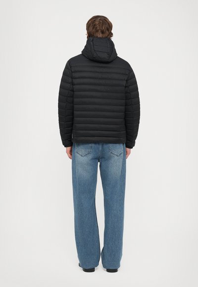 Doudoune noire avec des coutures horizontales, capuche et coupe décontractée. Associée à un jean bleu taille haute à jambes larges en denim.