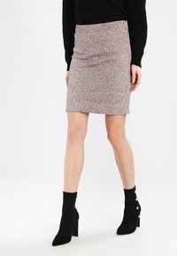 Jupe crayon en tricot rose clair avec une finition texturée. Taille haute, longueur genou. Assortie à des bottines noires qui présentent des accents dorés.