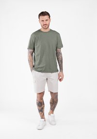 Olijfgroene T-shirt met ronde hals, gecombineerd met beige cargoshorts met zijzakken en witte sneakers.