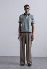 Kortærmet polo i lys grøn med zigzag mønster, sort krave, parret med beige vide bukser og sorte sko.