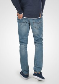 Lyseblå denimjeans med slim fit, med baklommer med subtil søm og en naturlig falming. Brukes med marineblå sneakers.