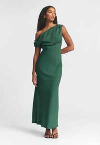 Zelené saténové maxi šaty s jedním ramínkem, s drapovaným materiálem na poprsí a elegantním, přiléhavým střihem. Minimalistické černé sandály.