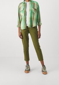 Zelená kostkovaná košile na knoflíky se dvěma kapsami na prsou, doplněná olivově zelenými zkrácenými kalhotami a šedými turistickými botami s oranžovými doplňky.