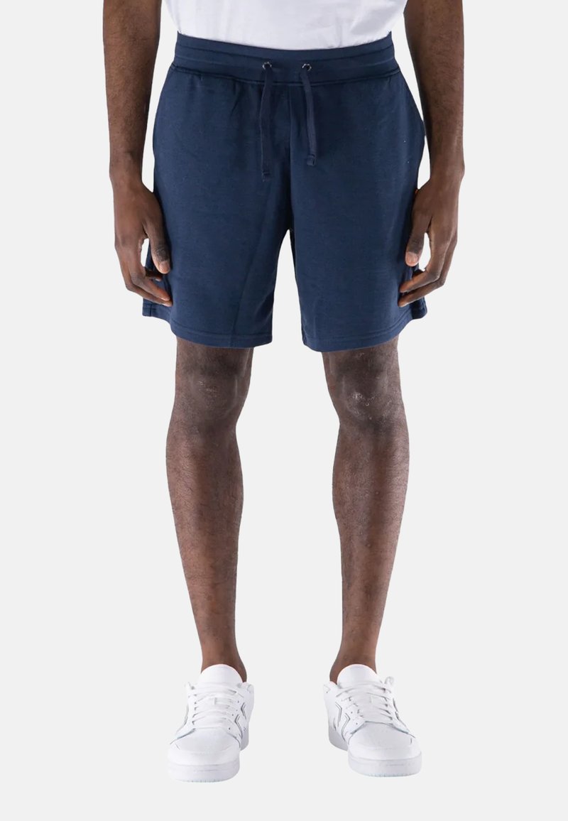 Pantaloni corti blu navy realizzati in un tessuto morbido, con vita regolabile con coulisse e tasche laterali. Indossati con sneakers bianche.
