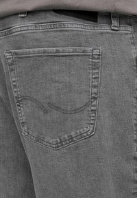 Gray denim jeans feature a back pocket with a subtle curved stitching detail. The texture is smooth with a slight sheen, providing a modern appearance.