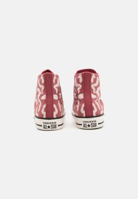 Baskets montantes en toile rose avec un motif abstrait blanc, semelle en caoutchouc noire, et logo Converse All Star à l'arrière.
